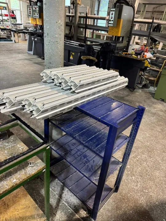 Cut white plastic window frame extrusions stacked on a blue metal table inside a manufacturing facility.