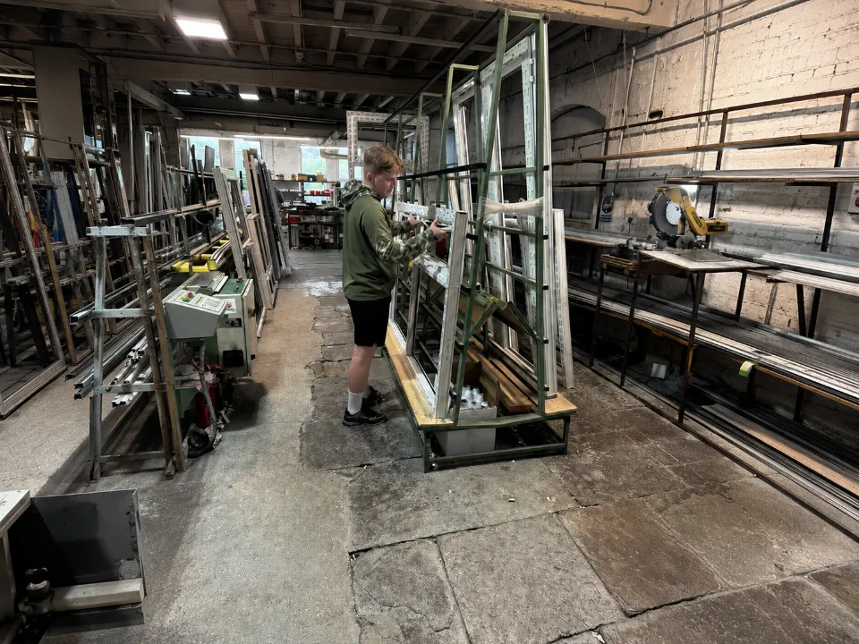 A worker inspecting white window frames resting on an A-frame storage rack in an industrial workshop.