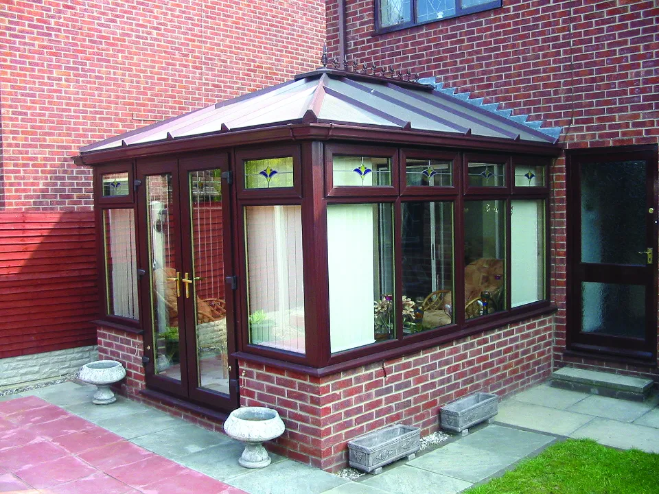 Dark reddish-brown uPVC conservatory with decorative stained glass accents on top windows, built on a brick base.
