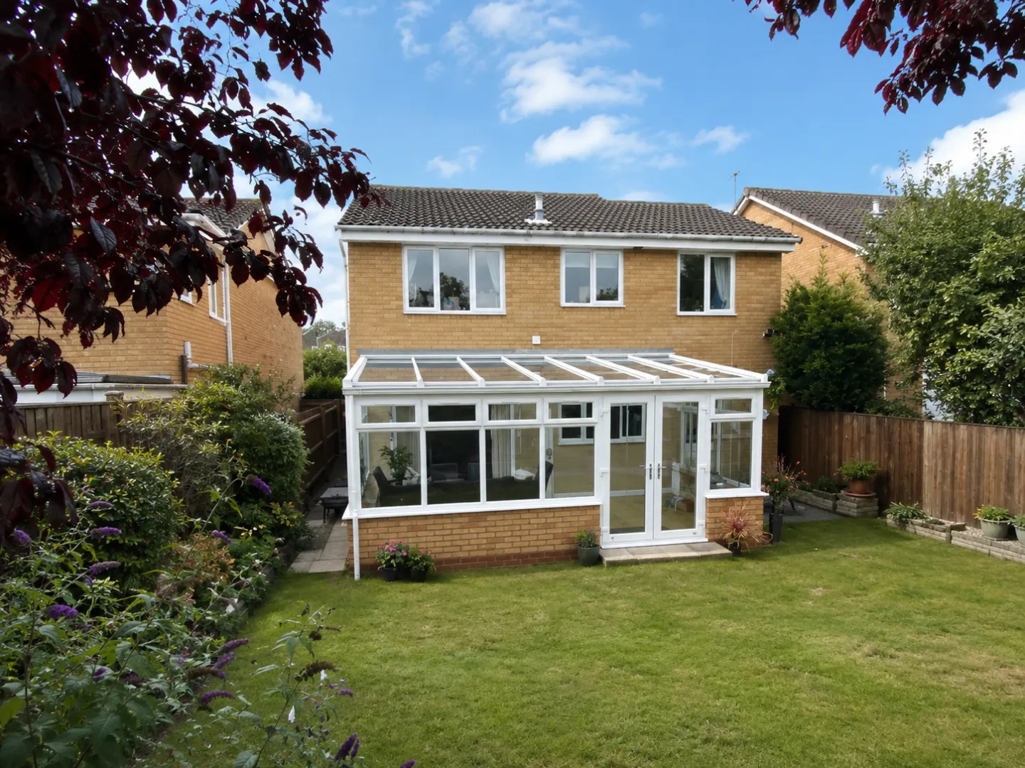 Exterior view of a white lean-to conservatory attached to the rear of a yellow brick house with a green lawn.