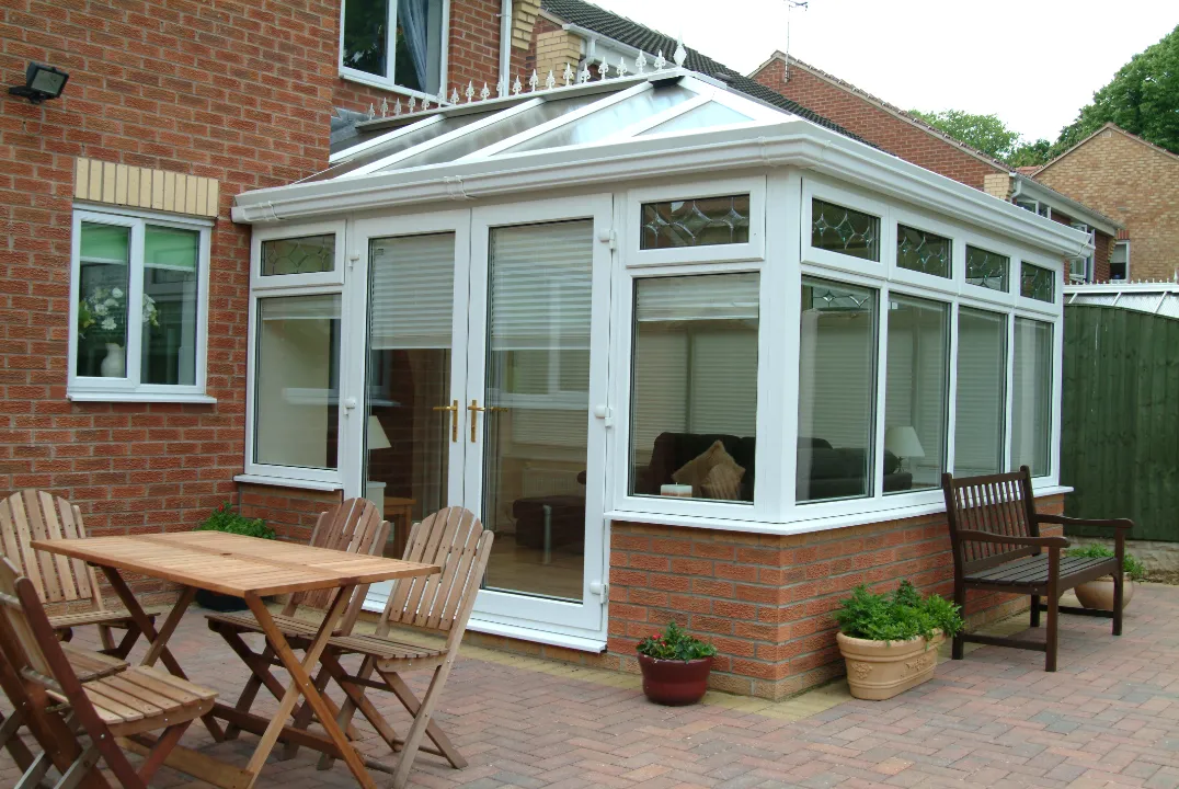 Exterior view of a white uPVC Edwardian-style conservatory with leaded top windows, attached to a brick home next to a patio table set.