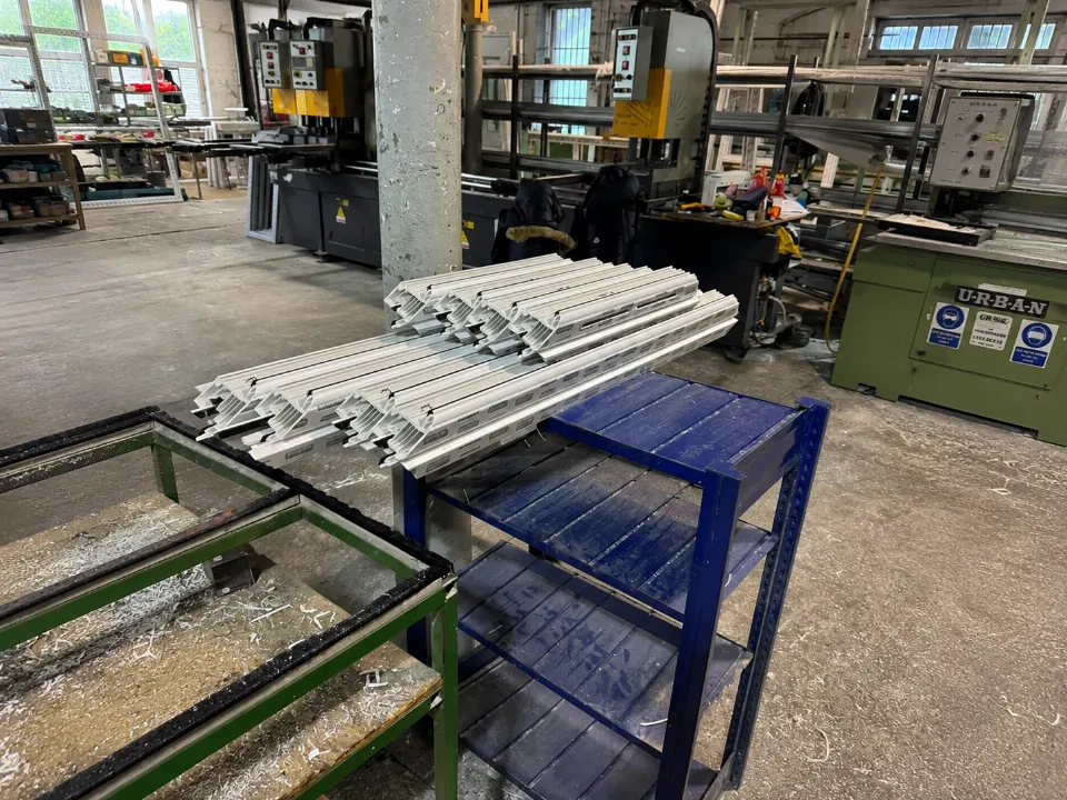 Cut white plastic window frame extrusions stacked on a blue metal table inside a manufacturing facility.
