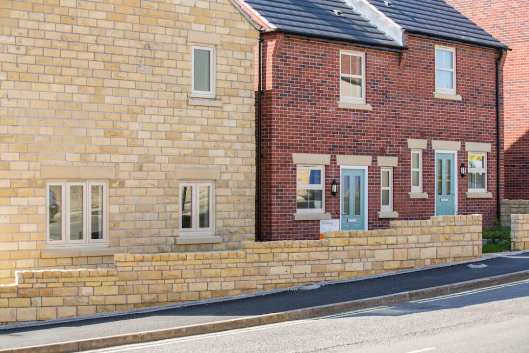 Modern terraced residential houses with stone and red brick facades, white UPVC flush windows, and a low stone wall along the sidewalk.