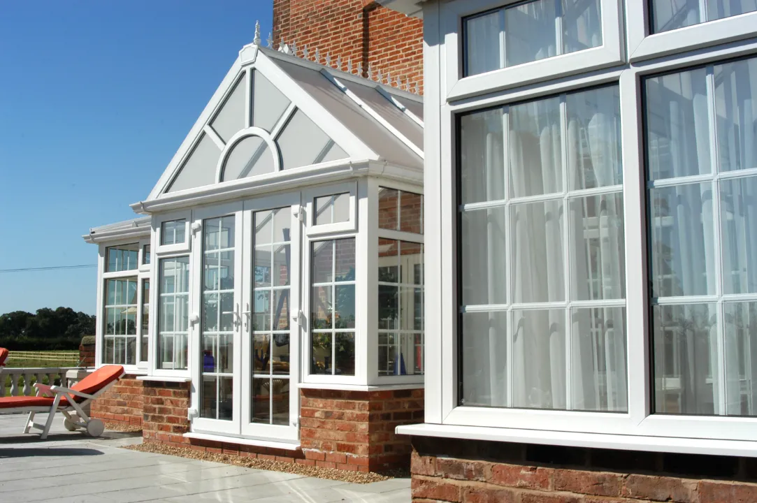 Exterior view of a white gable-front conservatory extension built on a red brick base next to a patio.