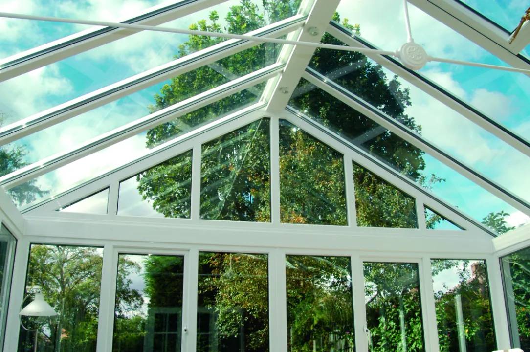 Interior view looking up at the vaulted glass roof and gabled window wall of a bright white conservatory.