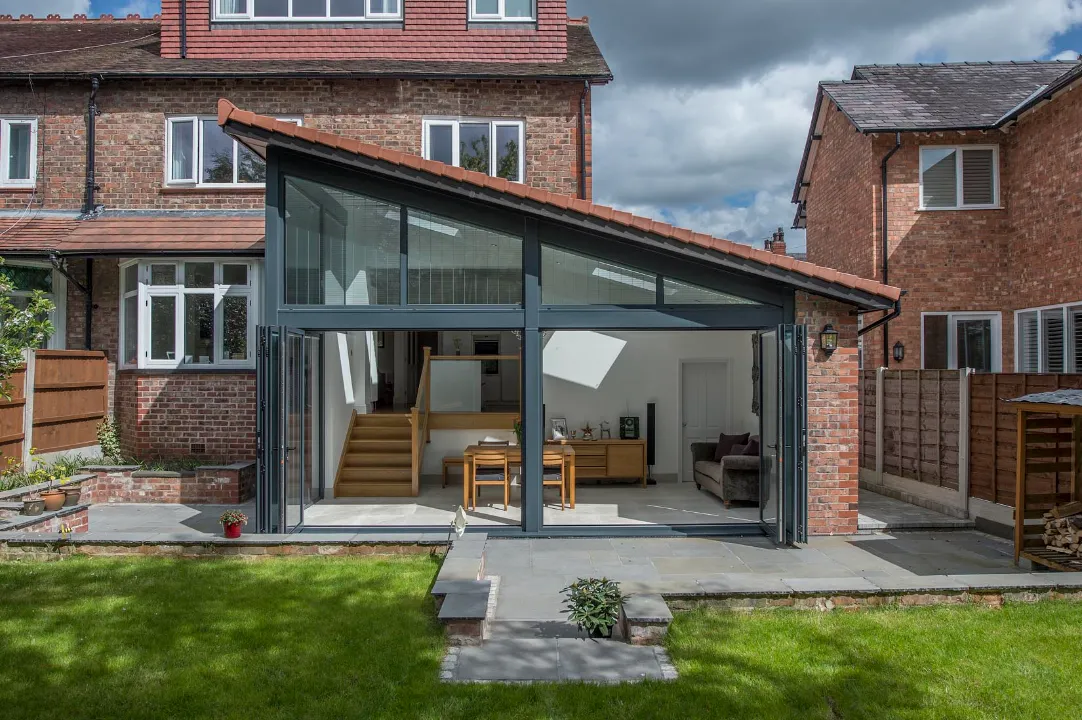 Exterior view of a modern brick home extension with a sloped roof and fully opened bi-fold glass doors facing a green garden.