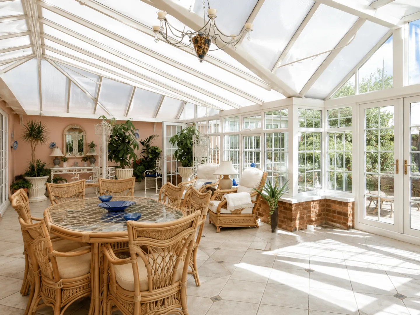 Interior view of a large white glass conservatory filled with natural light, tiled flooring, and wicker dining and seating furniture.