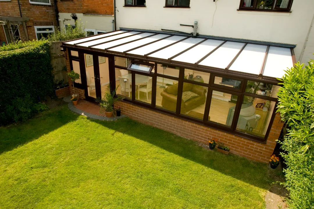 High-angle view of a dark wood lean-to conservatory extension with a glass roof overlooking a lush green lawn.