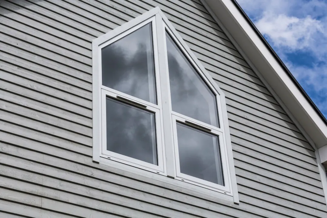 A white flush bespoke window installed on a grey horizontal siding wall.