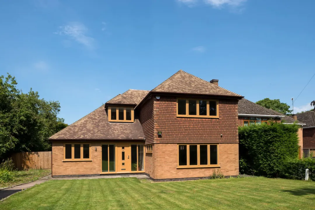 A two-story residential house with light wood-effect window frames, a matching front door, and a green lawn.