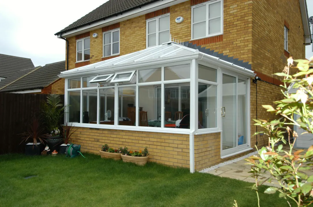 White lean-to conservatory extension with sliding glass doors on a yellow brick base, attached to a two-story home.