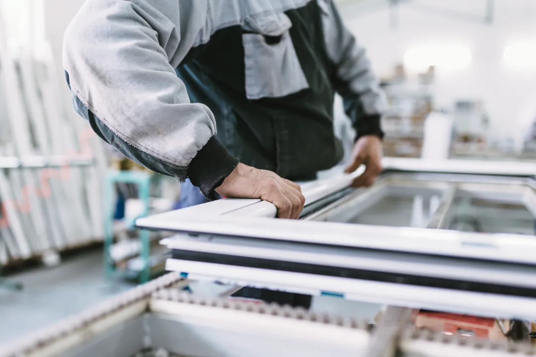 Close-up of a technician's hands carefully adjusting and assembling a white window sash on a factory production line.