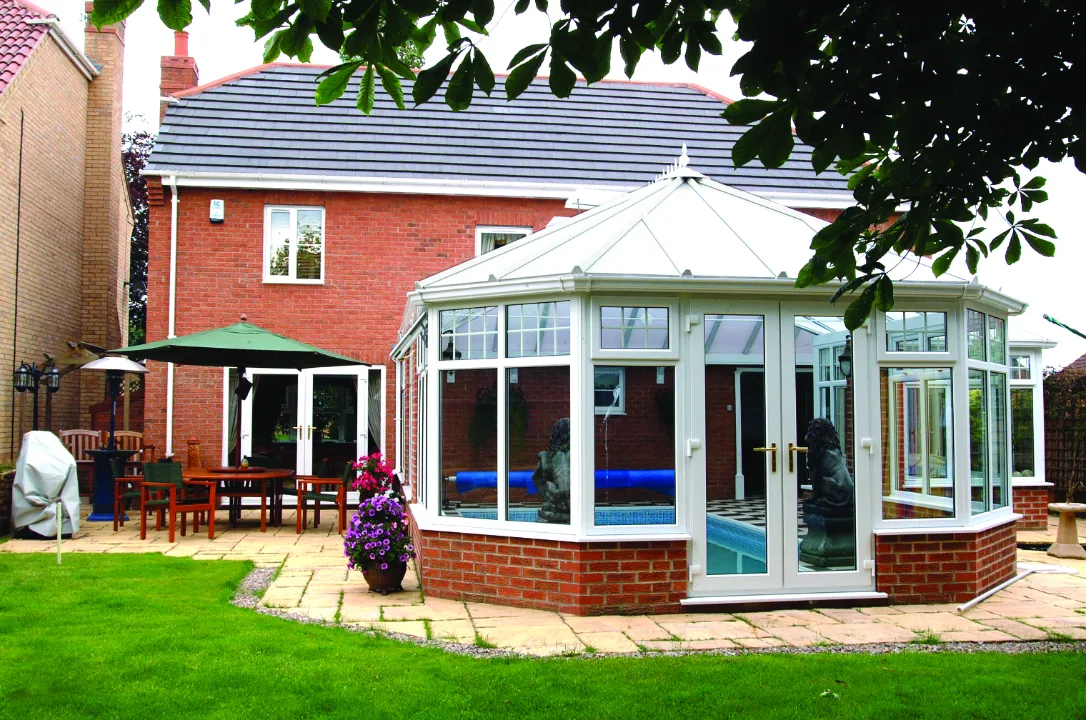 High-angle exterior view of a large white Victorian conservatory housing an indoor pool attached to a modern brick house.