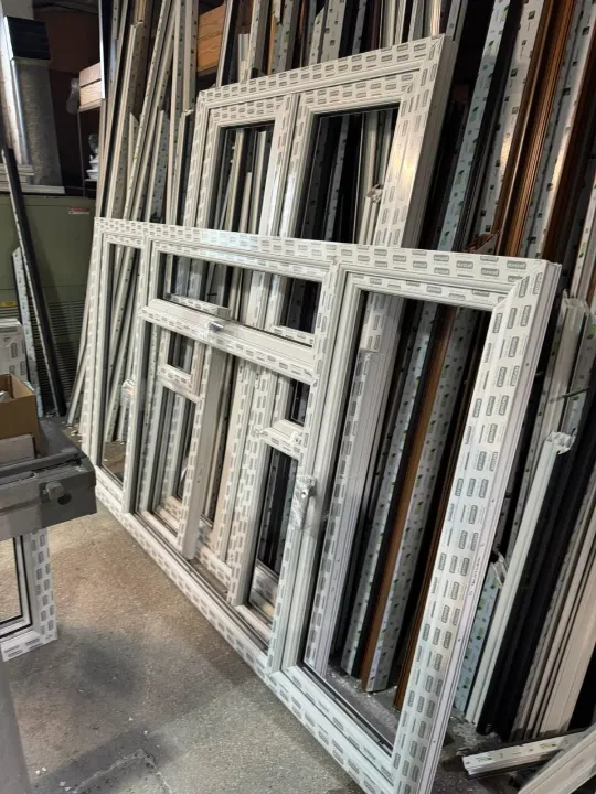 Finished white arched French doors and window frames stacked inside a factory workshop.
