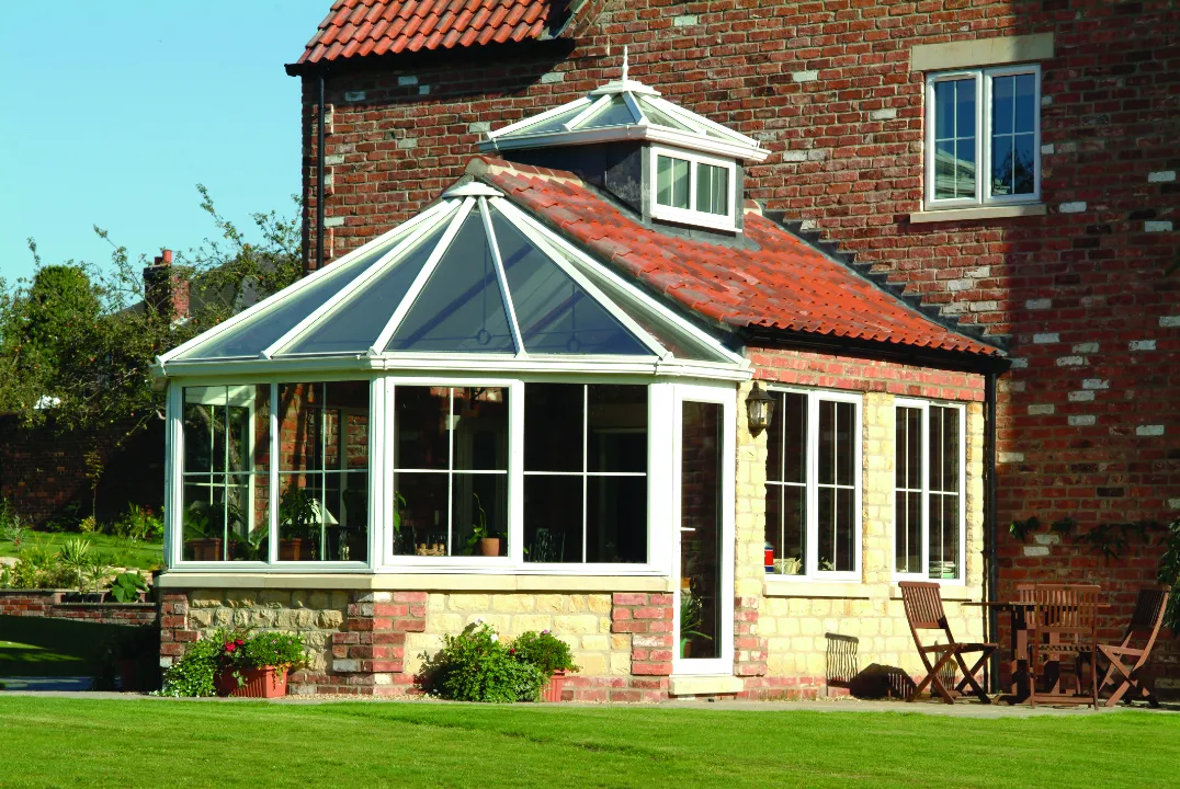 Close-up exterior view of a custom white conservatory with a tiled roof transition attached to a multi-story brick building.