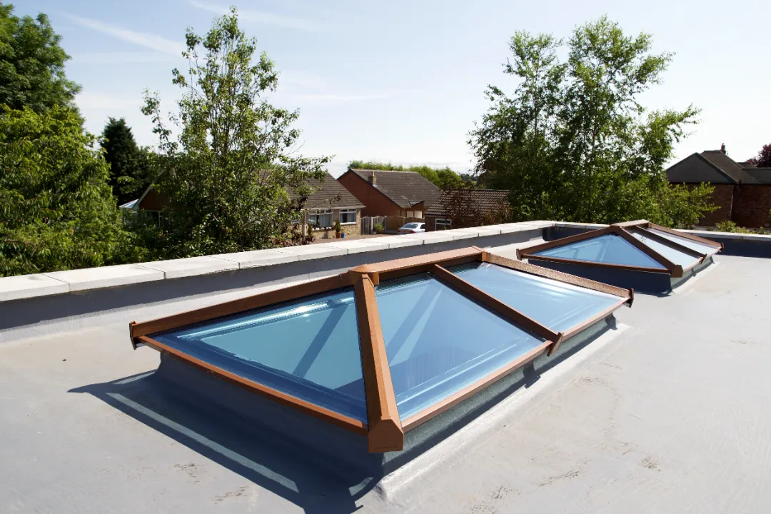 Close-up of two warm oak-effect roof lantern skylights fitted on a flat gray extension roof overlooking a residential neighborhood.