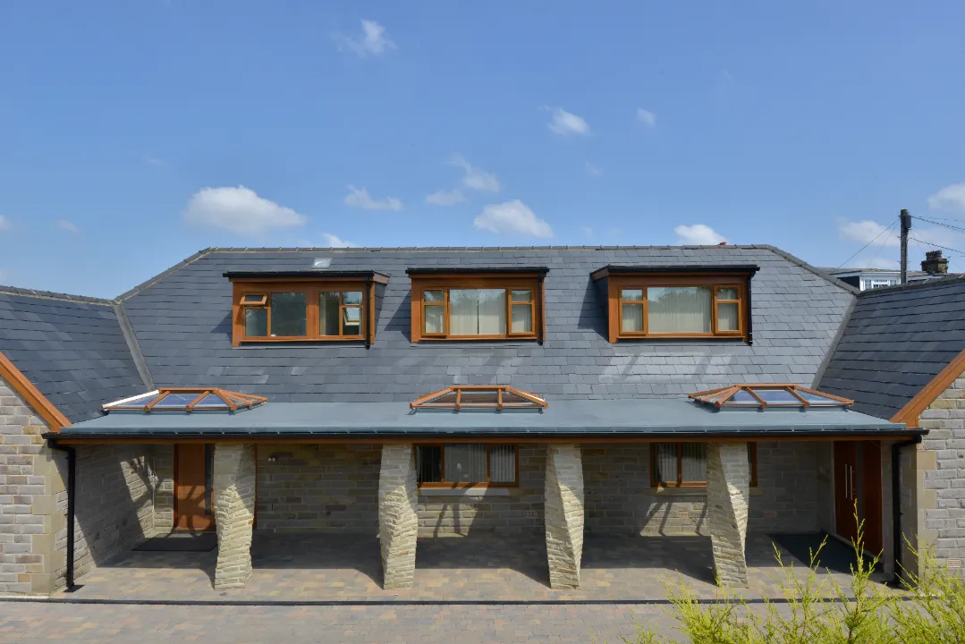 Exterior view of a stone house with slate roofing featuring a flat covered porch section installed with three oak-effect roof lanterns.
