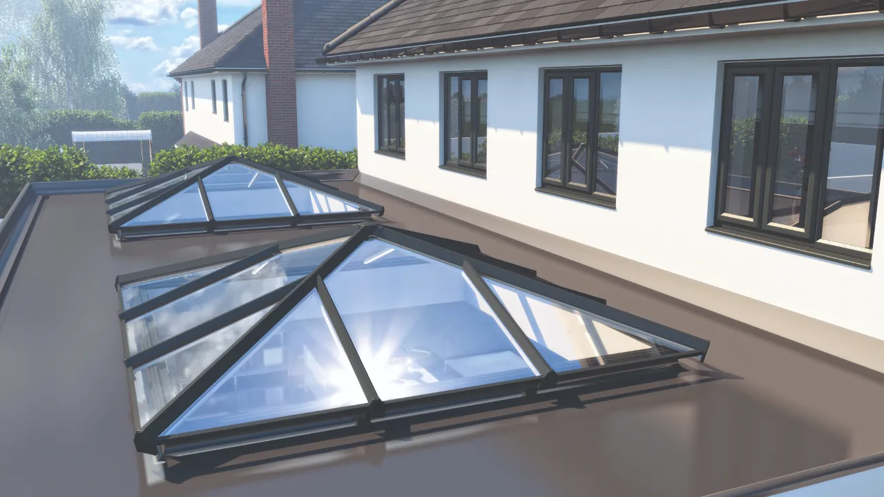 Close-up outdoor view of two black metal roof lantern skylights mounted on a gray flat roof addition next to a white residential building.