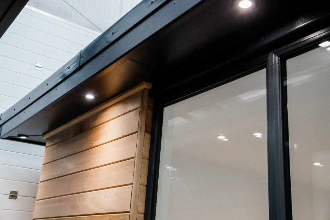 Close-up of a modern garden room overhang featuring dark soffits with recessed downlights and light wood horizontal cladding next to a glass door.