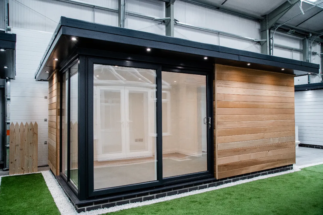 Exterior view of a contemporary garden room featuring natural wood cladding, black metal framing, large glass windows, and roof spotlights.