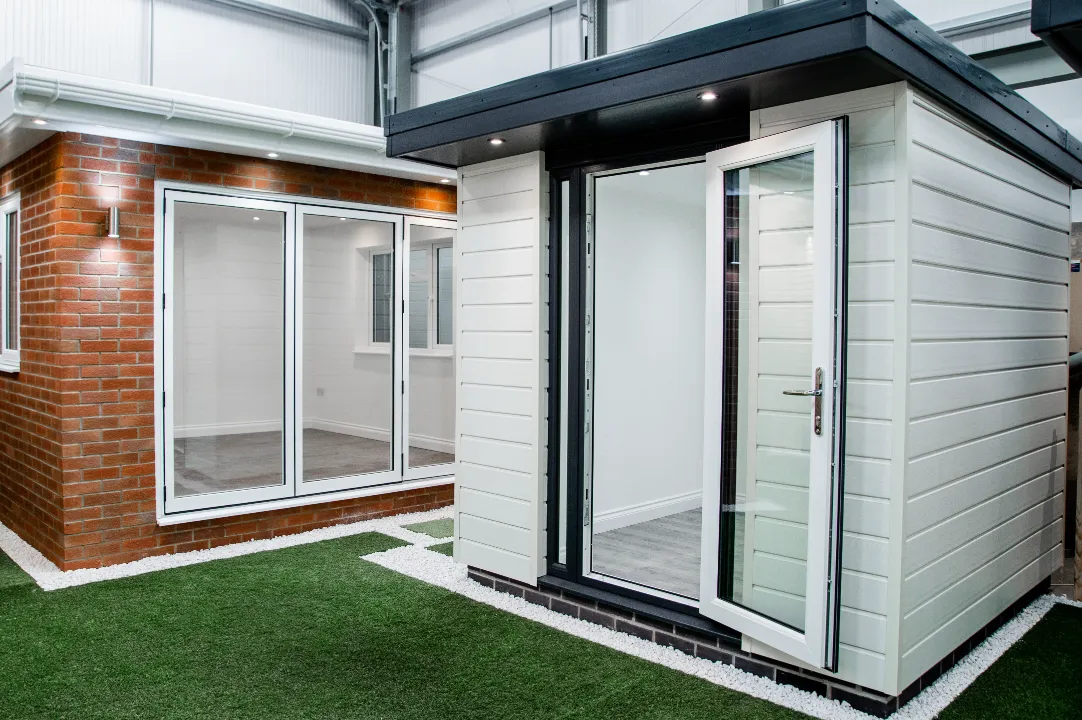 White horizontal-clad garden room pod with a glass door sitting next to a brick-clad display garden room in an indoor showroom.