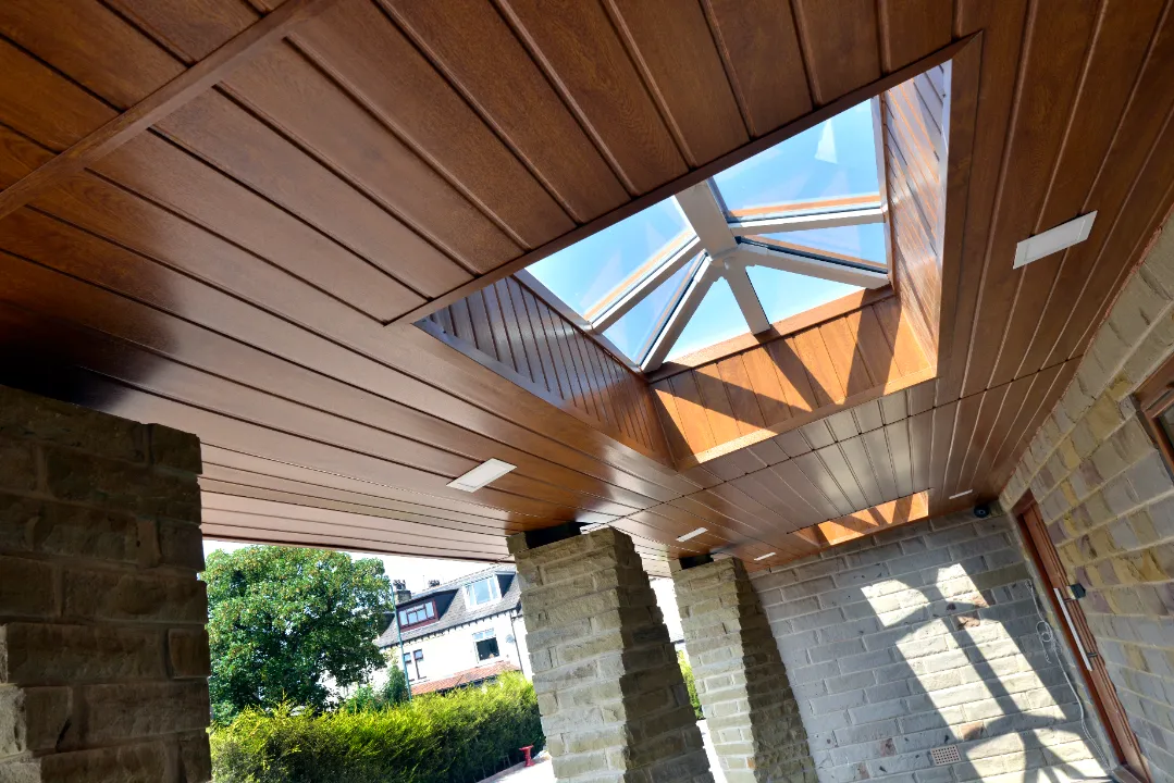 Low-angle view of a wooden covered patio ceiling featuring integrated flat light panel fixtures and a square glass roof lantern.